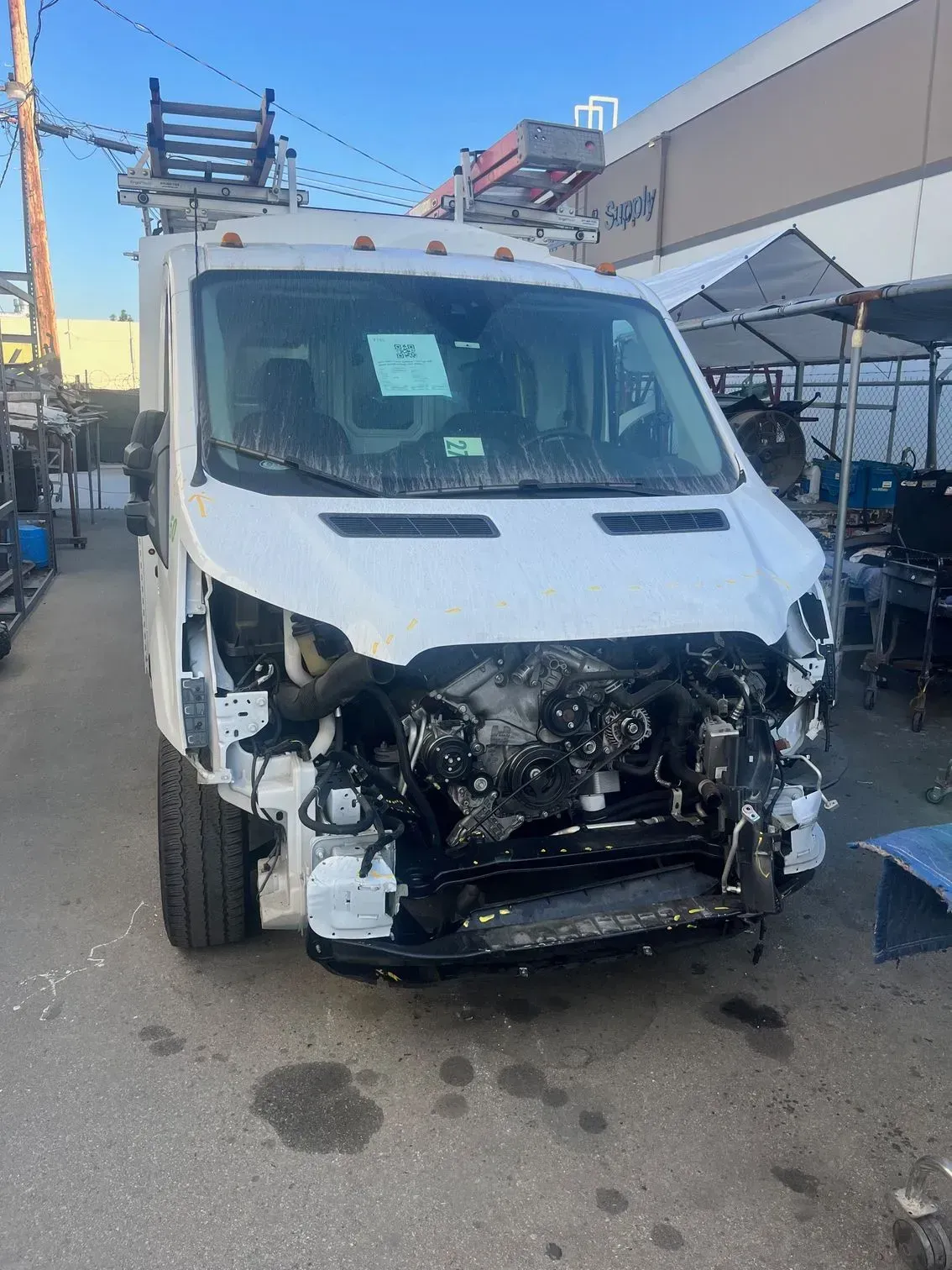 White cargo van with front-end damage; appears to be in a repair yard.