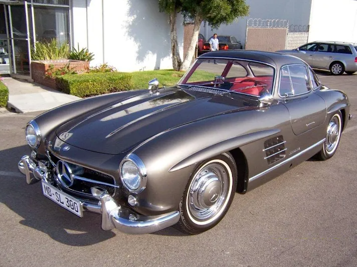 Gray Mercedes-Benz 300SL Gullwing coupe with red interior, parked outside a building.