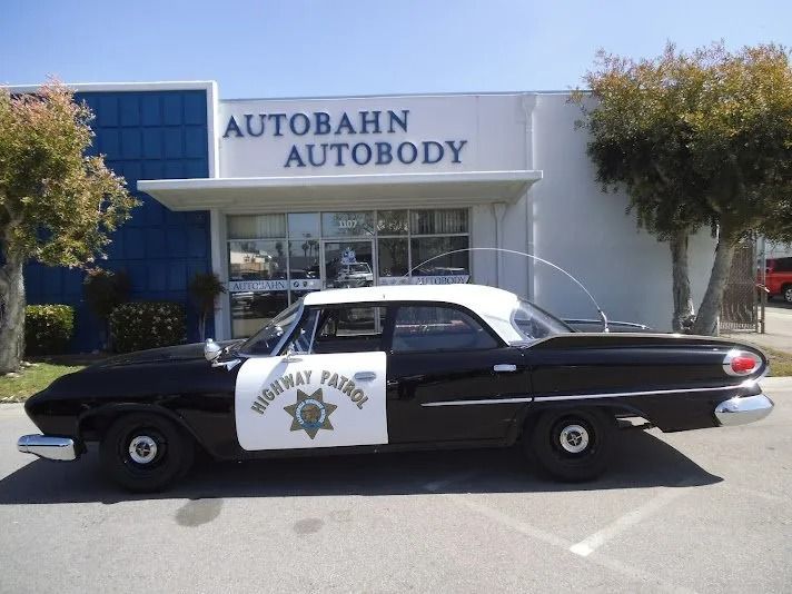 Black and white vintage highway patrol car parked in front of Autobahn Autobody building.