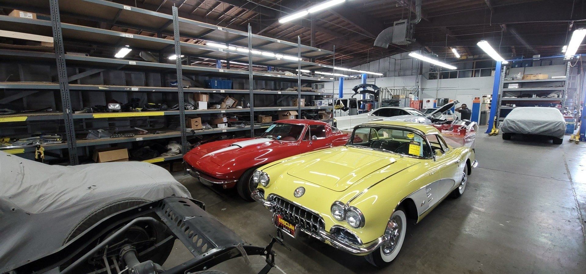 A yellow and red classic car in a large garage with storage shelves.