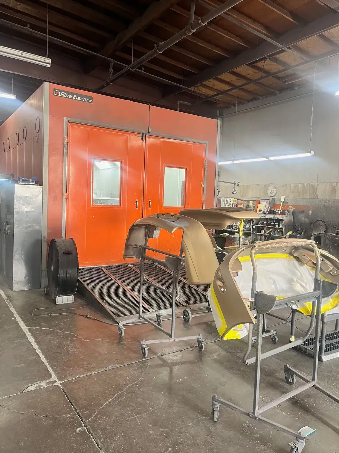 Orange paint booth in a workshop, with car parts on racks.