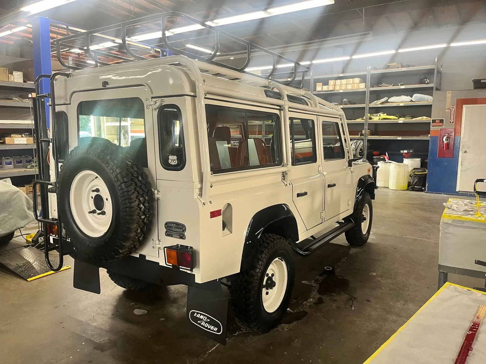 White Land Rover Defender SUV, black ladder on back, parked inside a garage.