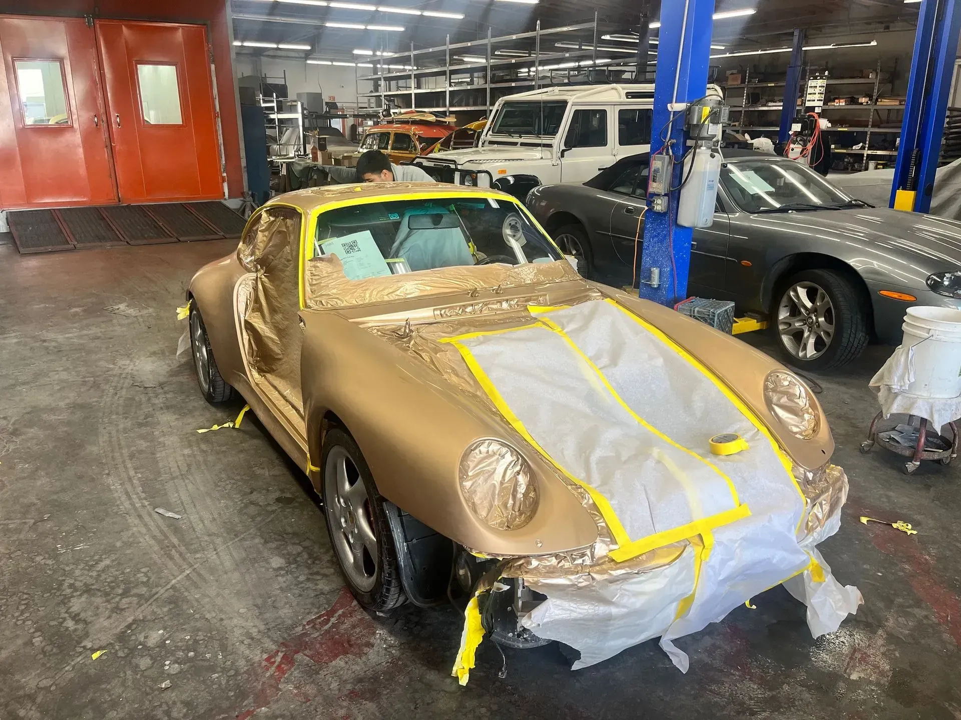 Gold Porsche 911 partially masked for paint in a repair shop.