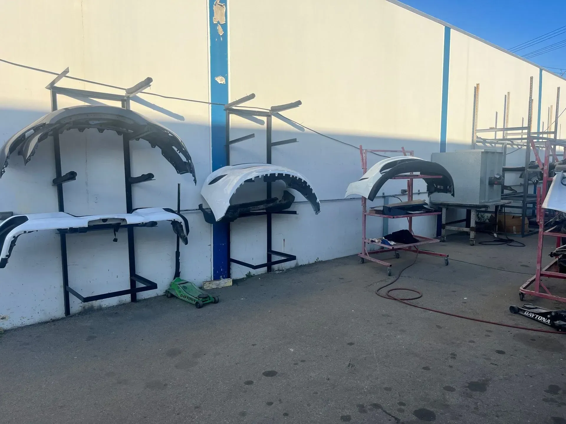 Car bumpers on stands outside a building. White and black automotive parts.