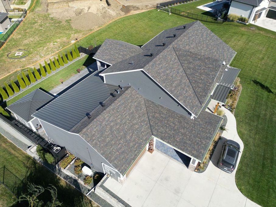 Aerial view of a gray roofed house with a black car in the driveway and green lawn.