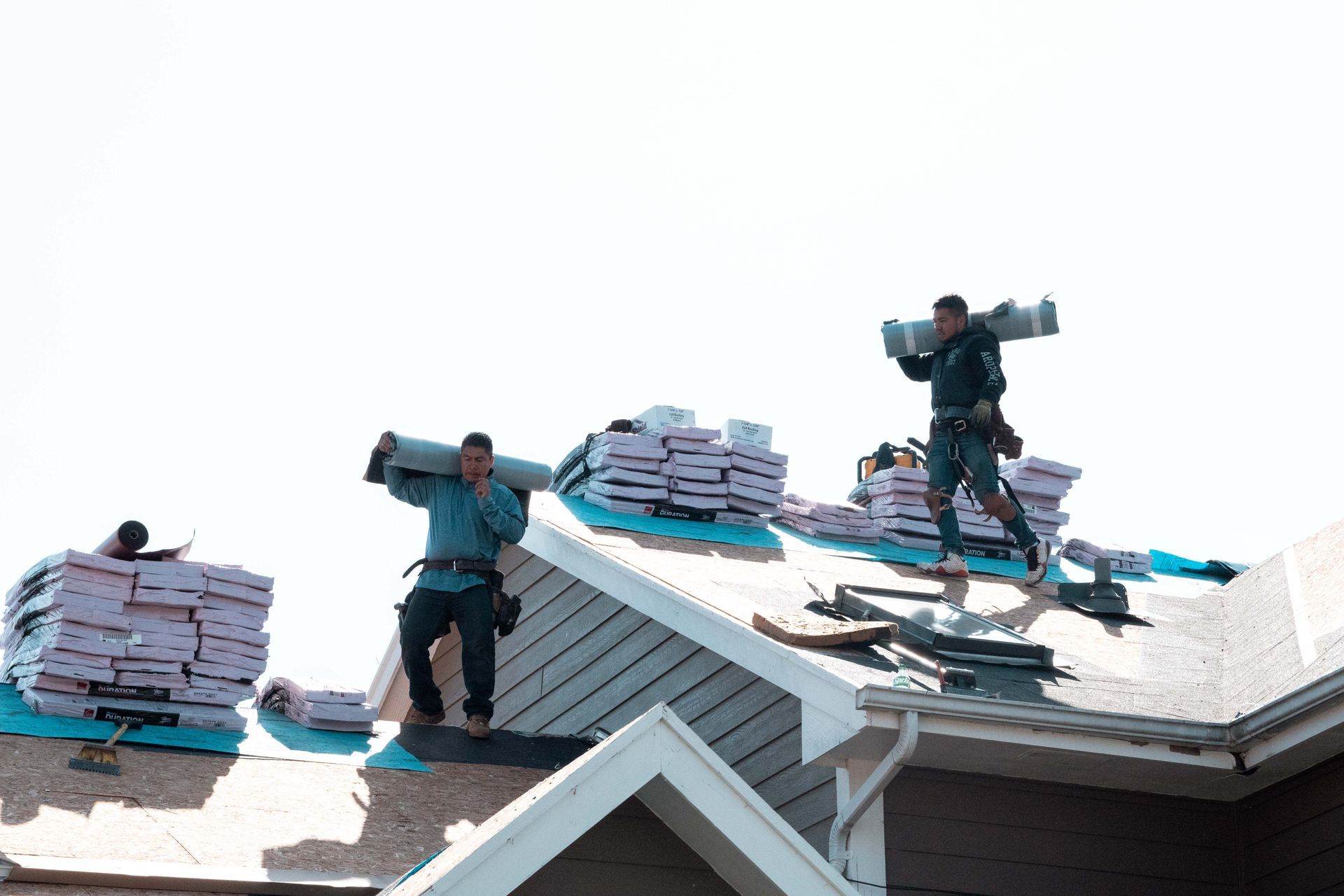 Roofers carrying materials on a roof, working in the sunlight.