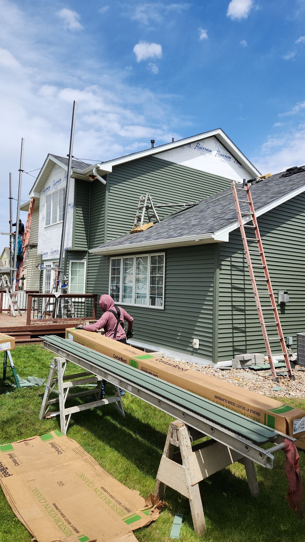 House exterior undergoing siding installation. Green siding, blue sky, construction materials, worker on ladder.