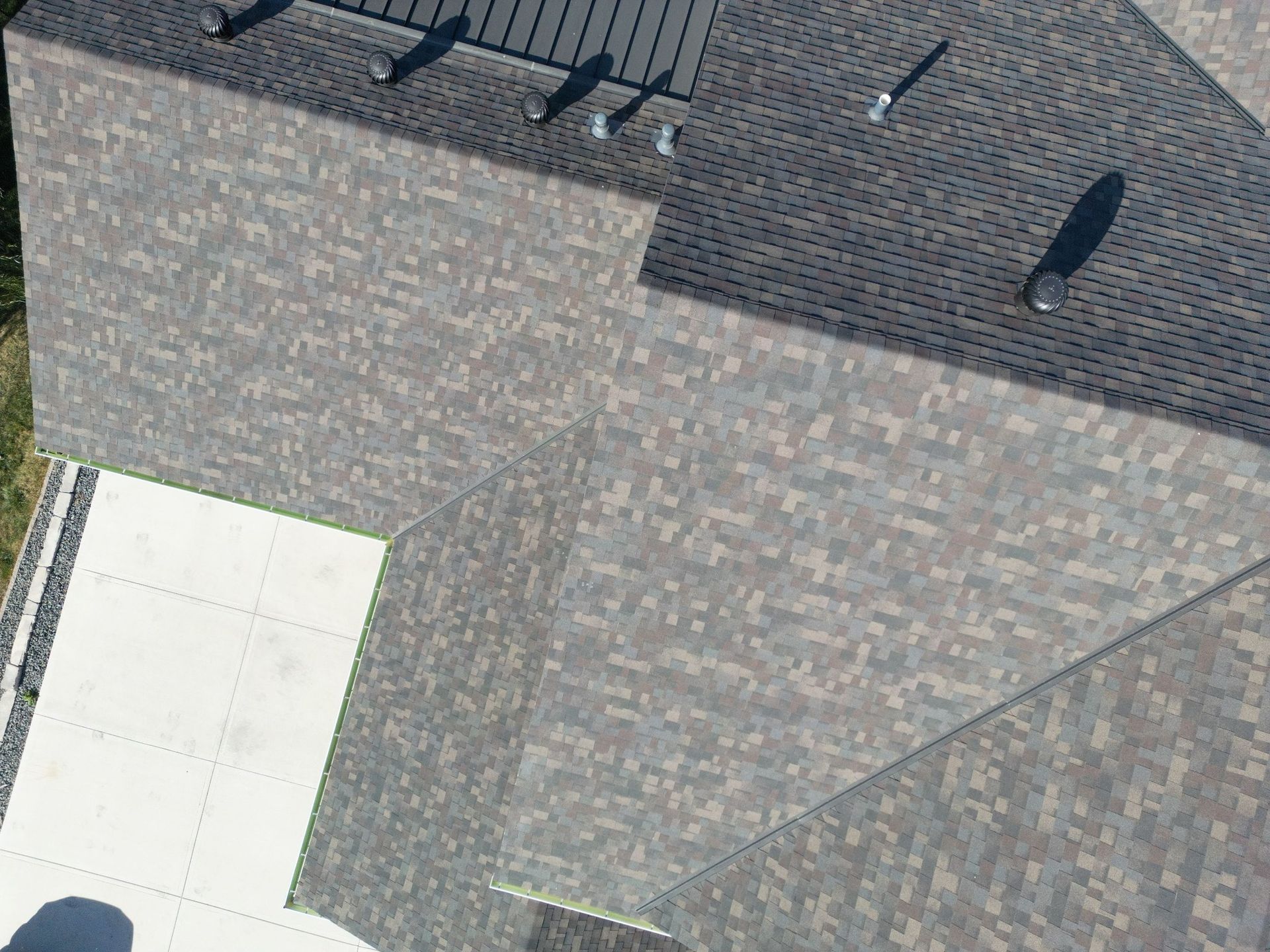 Overhead view of a house roof with dark shingles and several vents.
