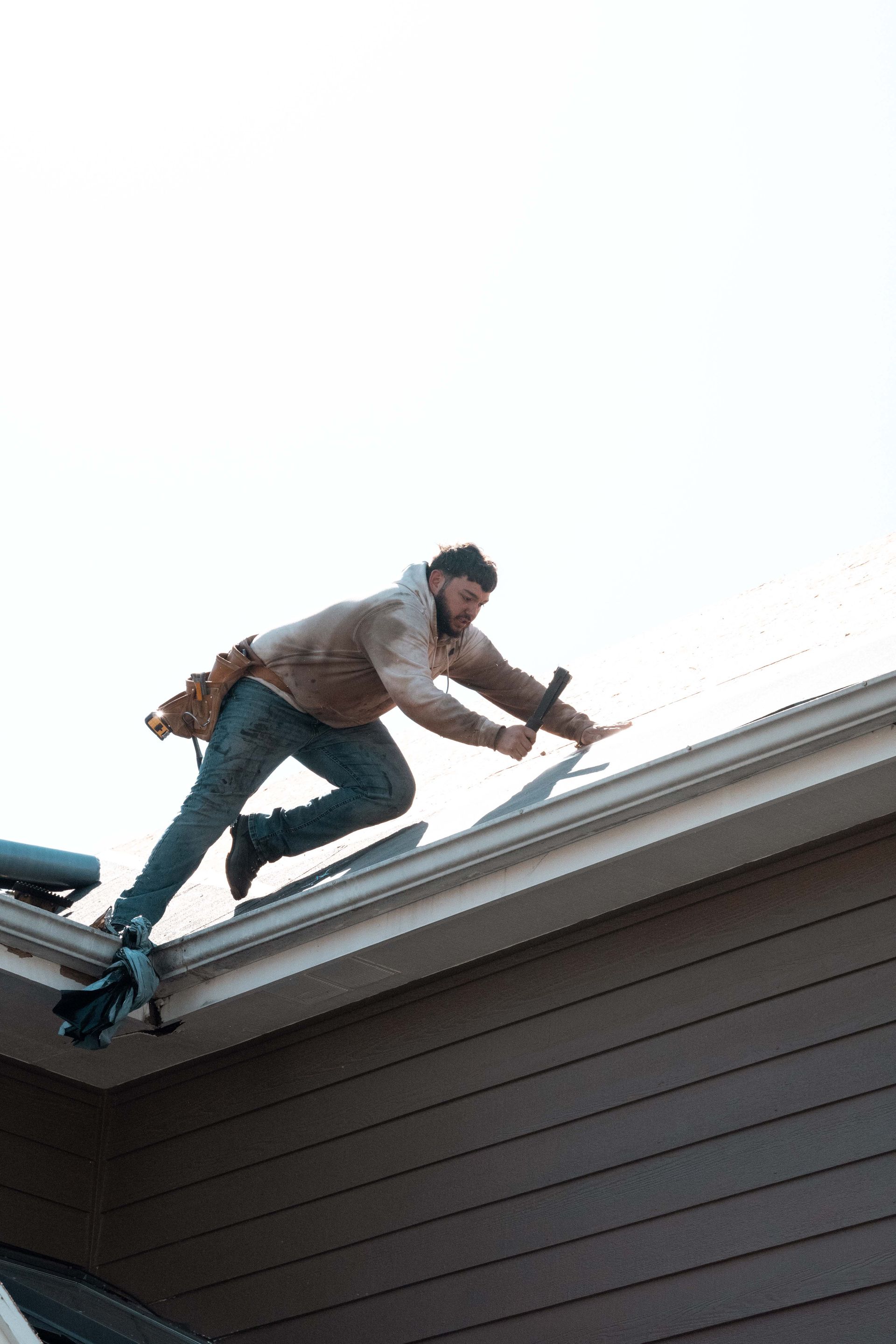 Roofer working on a roof, leaning, holding a hammer, clear sky.