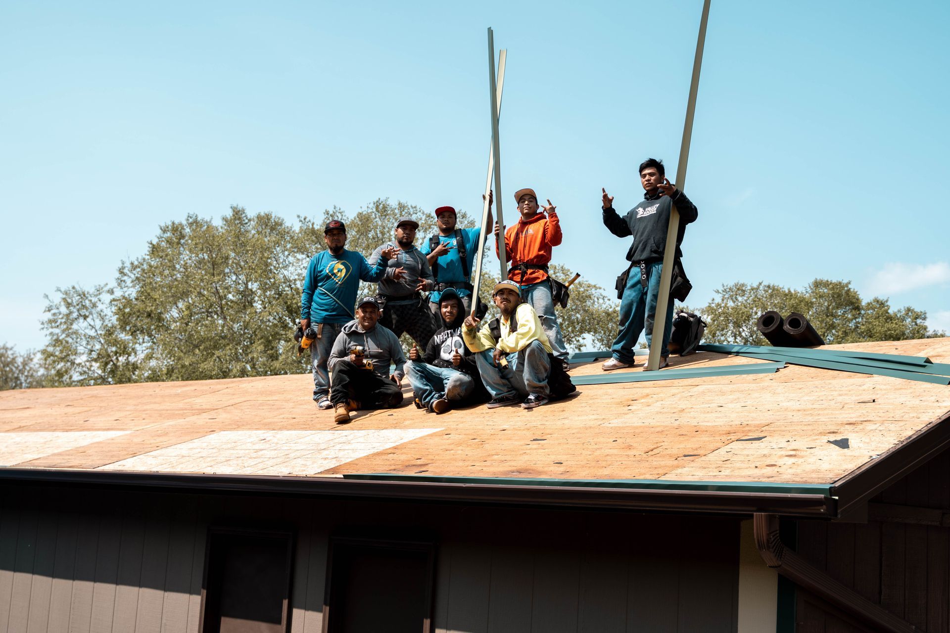 Group of people posing on a rooftop, with a blue sky background. Some are holding tools and smiling.