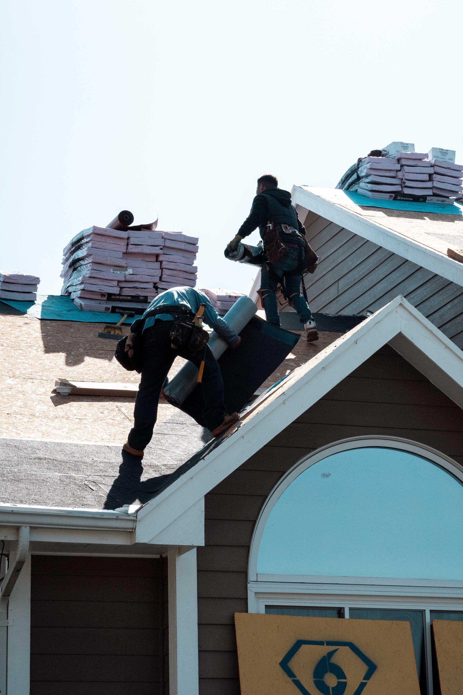 Construction workers installing roofing materials on a house under a sunny sky.
