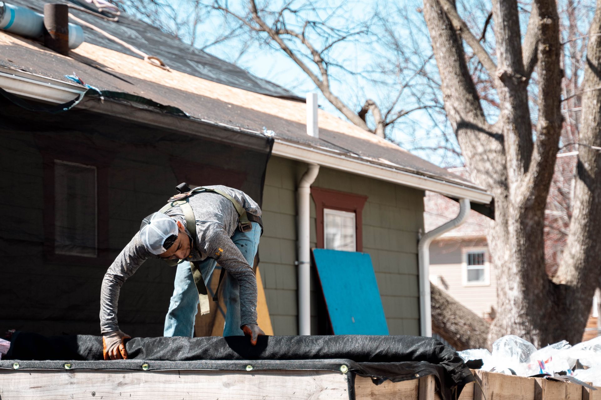 Roofer installing a black underlayment on a house roof. Blue sky, brown house with white trim.