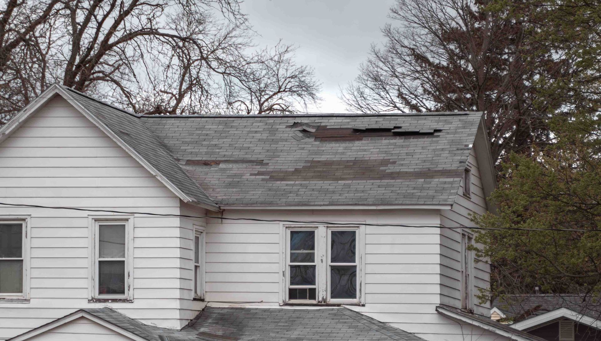 White house with damaged, weathered roof under overcast sky.