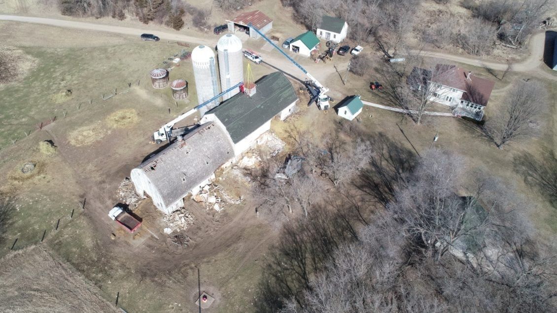 An aerial view of a farm with a barn and silos in the middle of a field