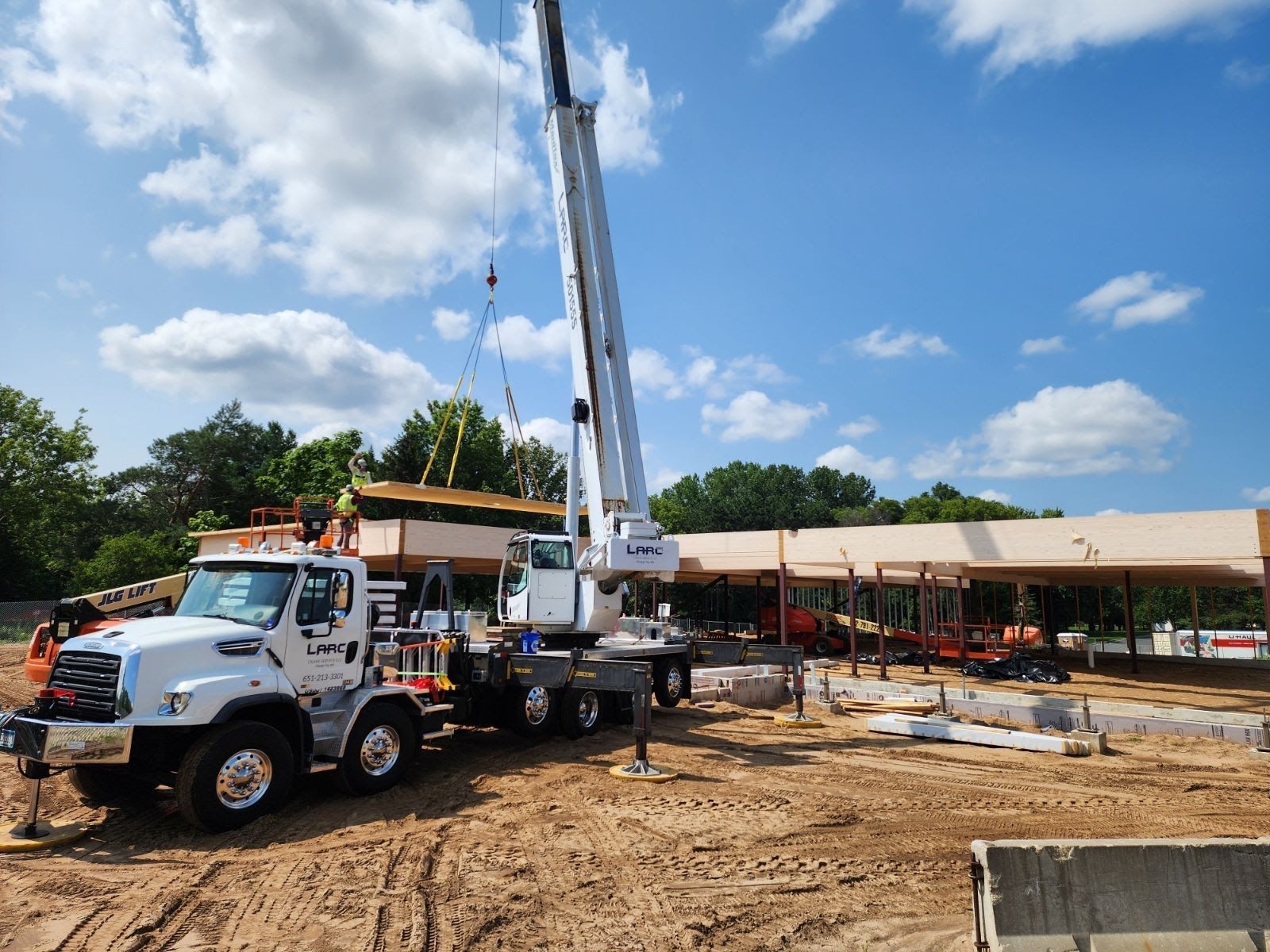 A truck with a crane attached to it is parked in front of a building under construction