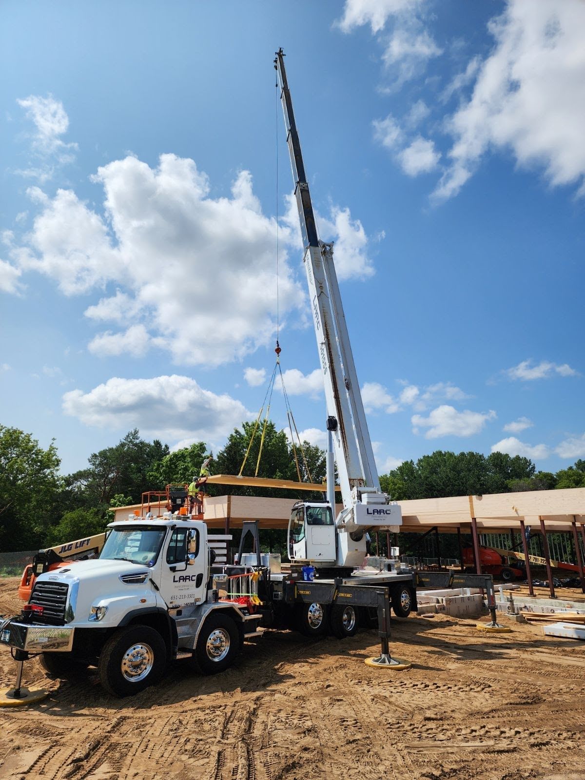 A large white truck with a crane attached to it is parked in a dirt field