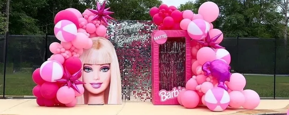 Barbie-themed pool party decorations: pink balloons, cardboard Barbie head, and box backdrop.