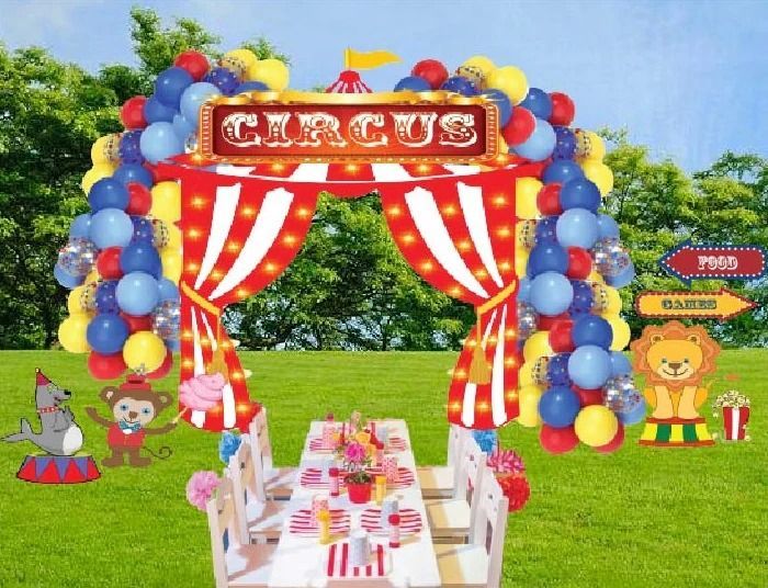 Circus-themed party setting with a balloon arch, tables, and cartoon animal decorations on grass.