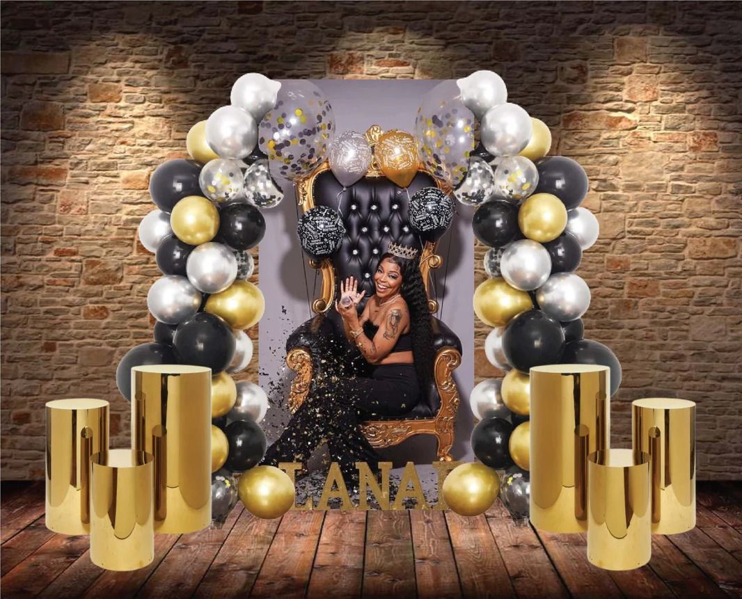 Birthday setup: Person in a black throne, surrounded by balloons and gold cylinders.