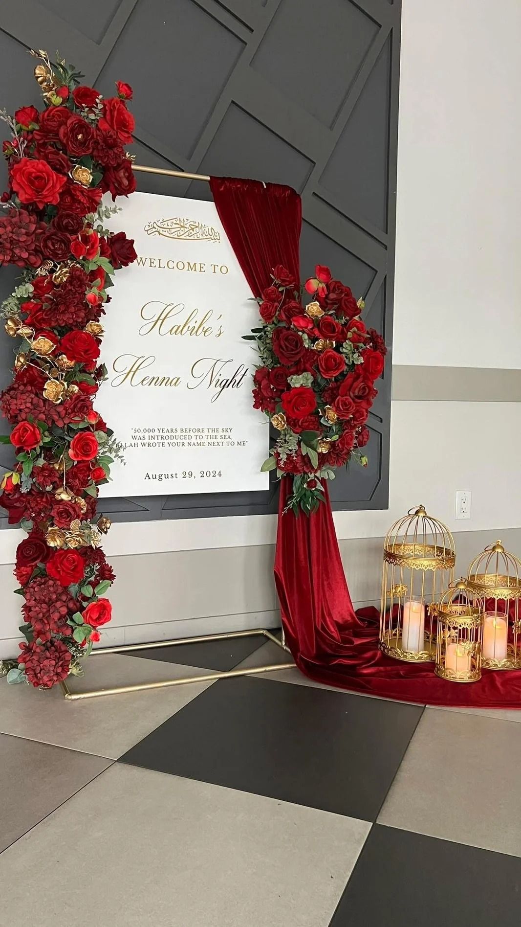 Elegant wedding sign with red floral arrangements and gold accents.