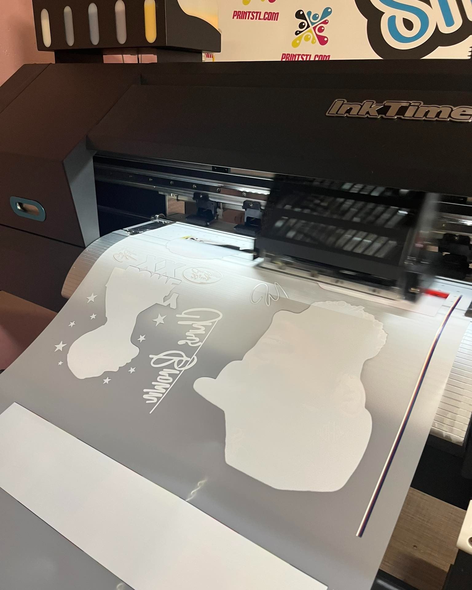 A printer printing white die-cut stickers. The stickers have shapes of a cat, star, and a cursive 