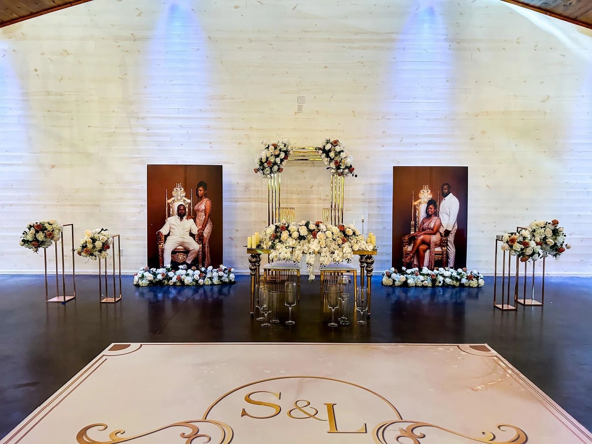 Wedding reception setup with gold accents and floral arrangements. Includes couple's portraits and a dance floor.