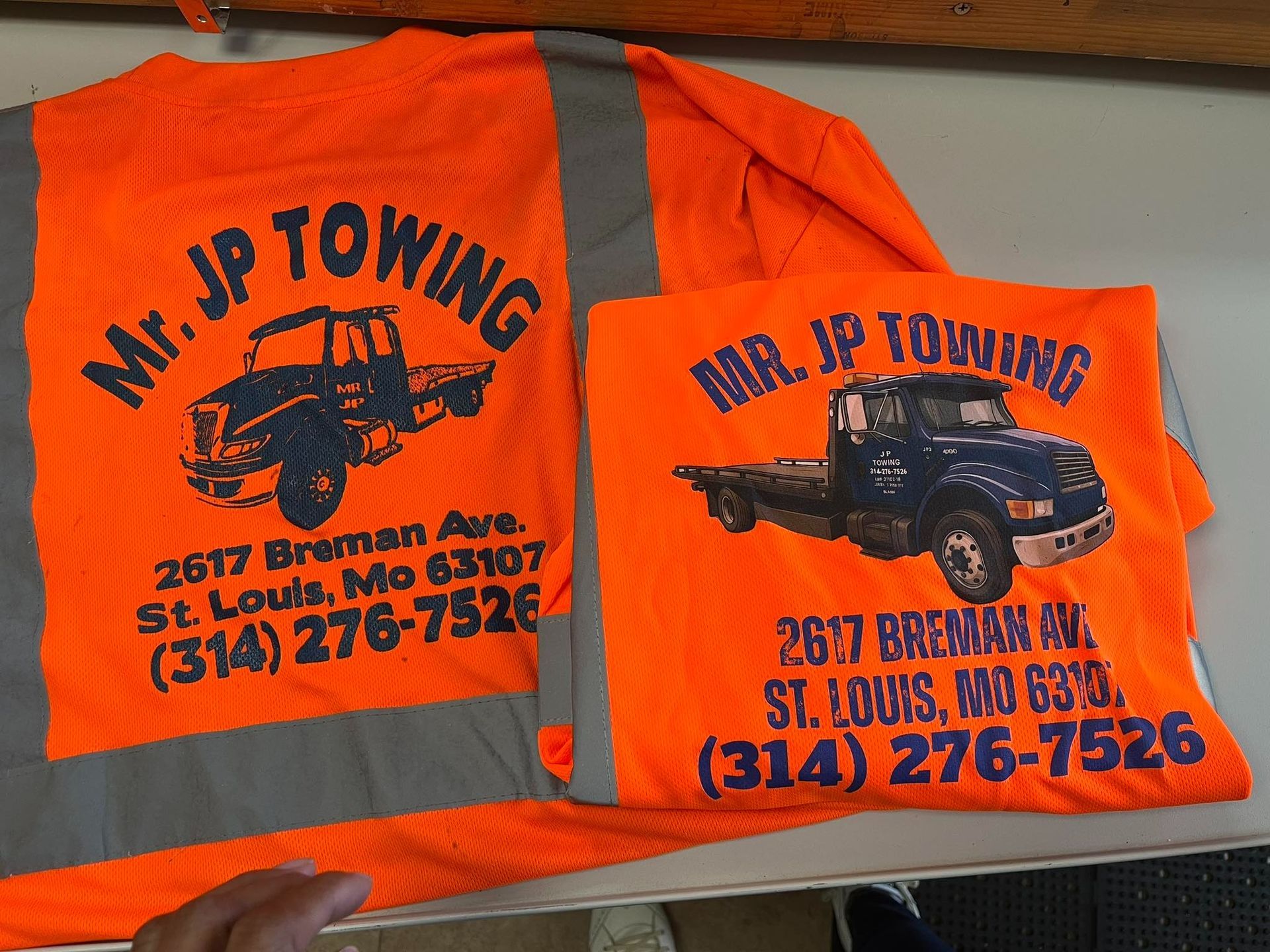 Two orange Mr. JP Towing shirts with truck logos and contact info.