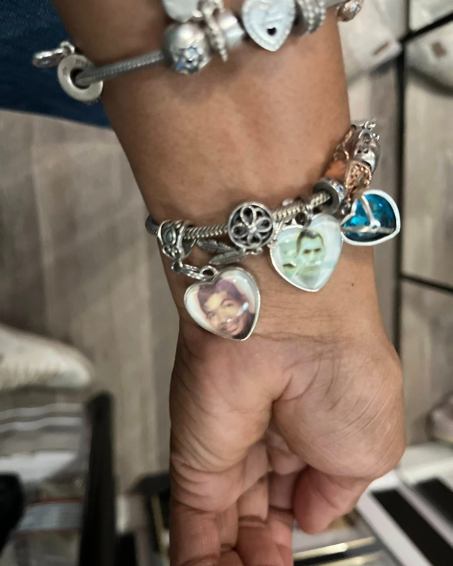 A person's wrist wearing a charm bracelet with heart-shaped photo charms and other decorative beads.