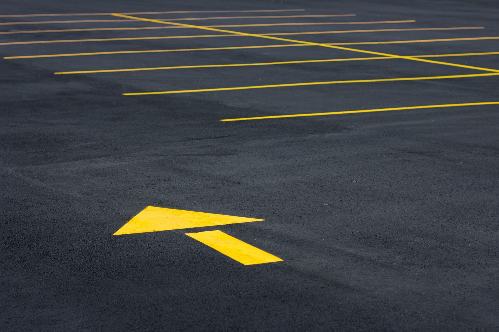 Yellow arrow on asphalt points right, indicating direction in a parking lot. Yellow parking space lines visible.