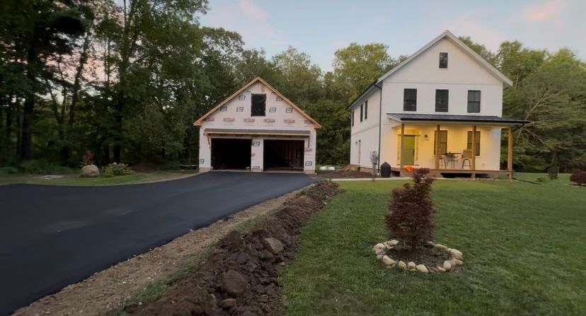 White farmhouse and attached garage with asphalt driveway and landscaping.
