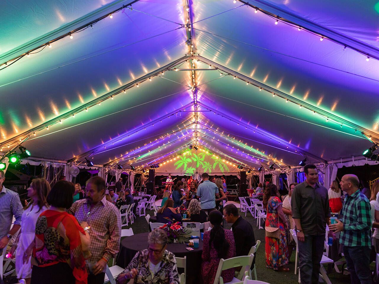 A group of people are standing under a tent with purple and green lights.