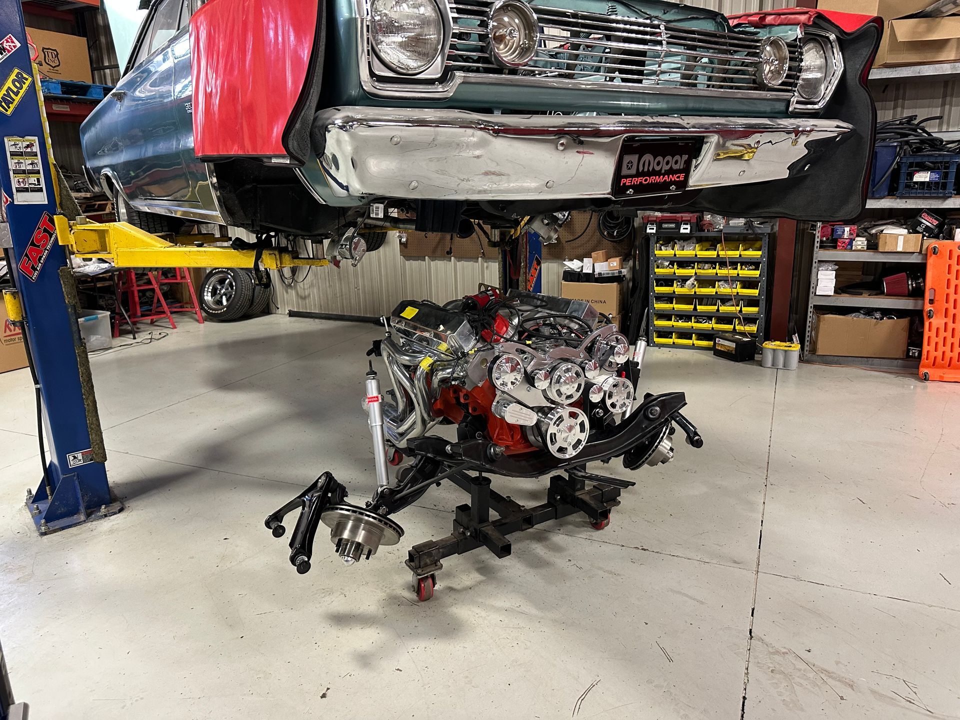 A car engine is sitting on a stand underneath a car in a garage.