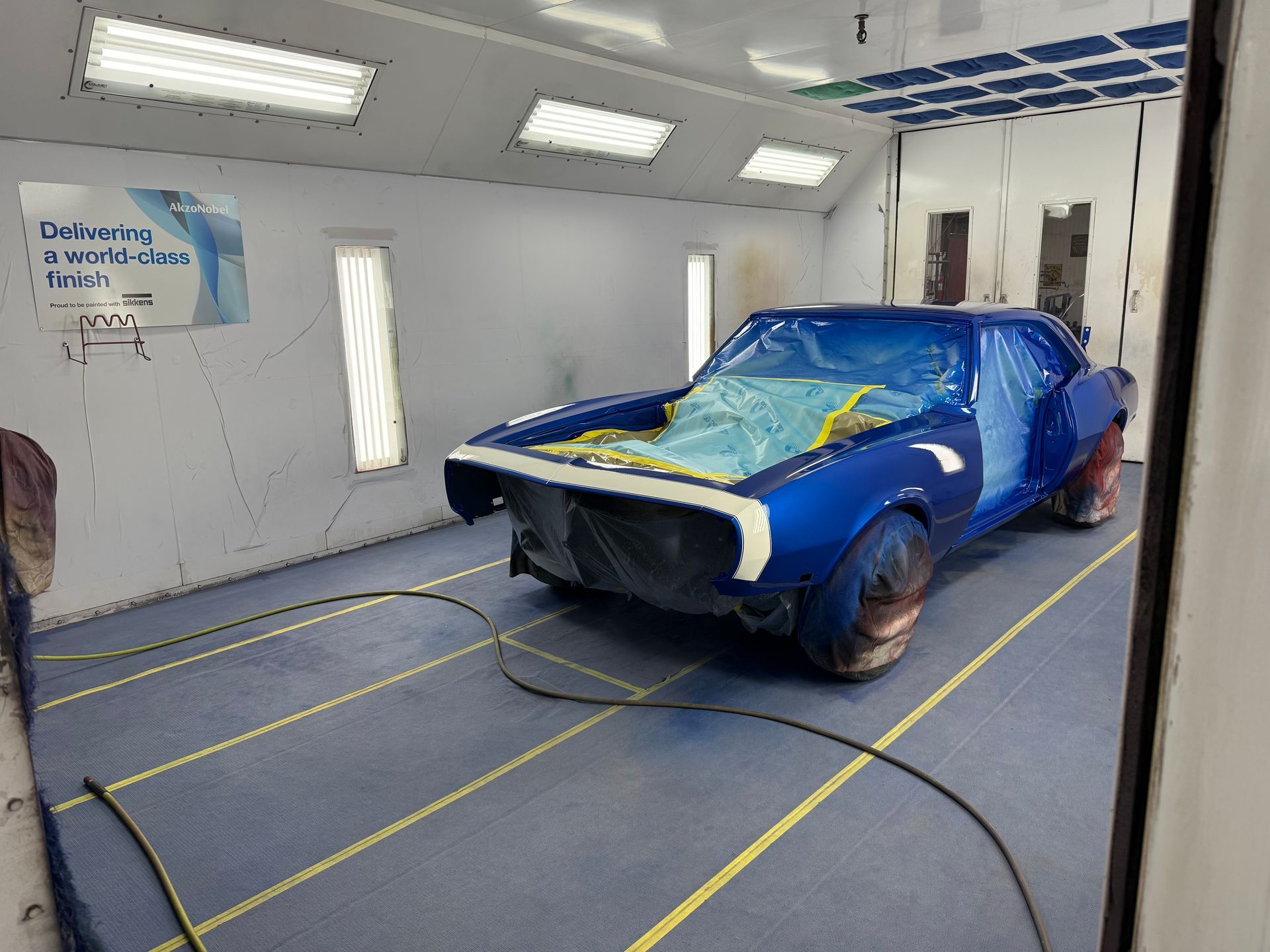 A blue car is being painted in a paint booth.