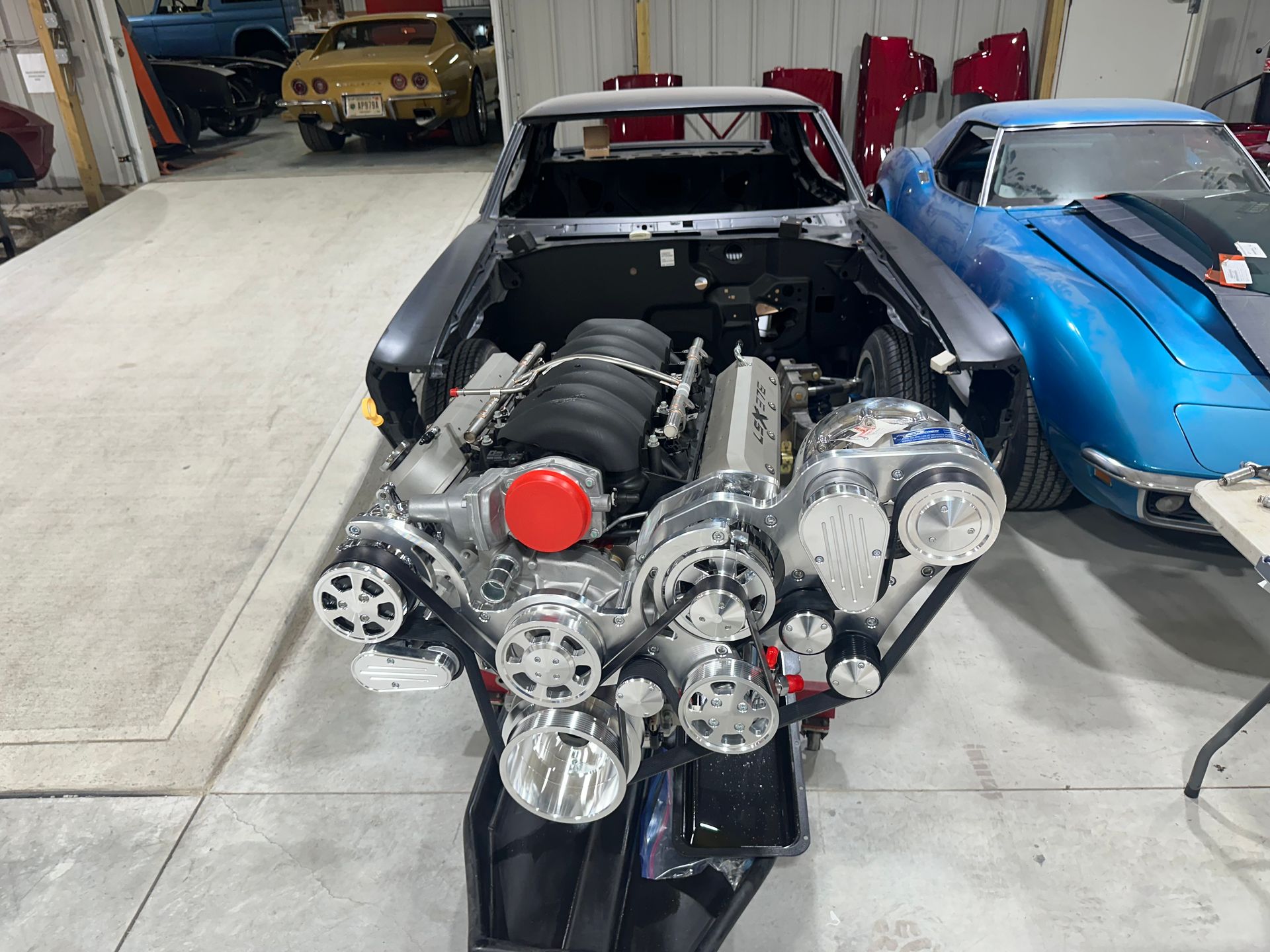 A car with the engine removed is sitting in a garage next to a blue car.