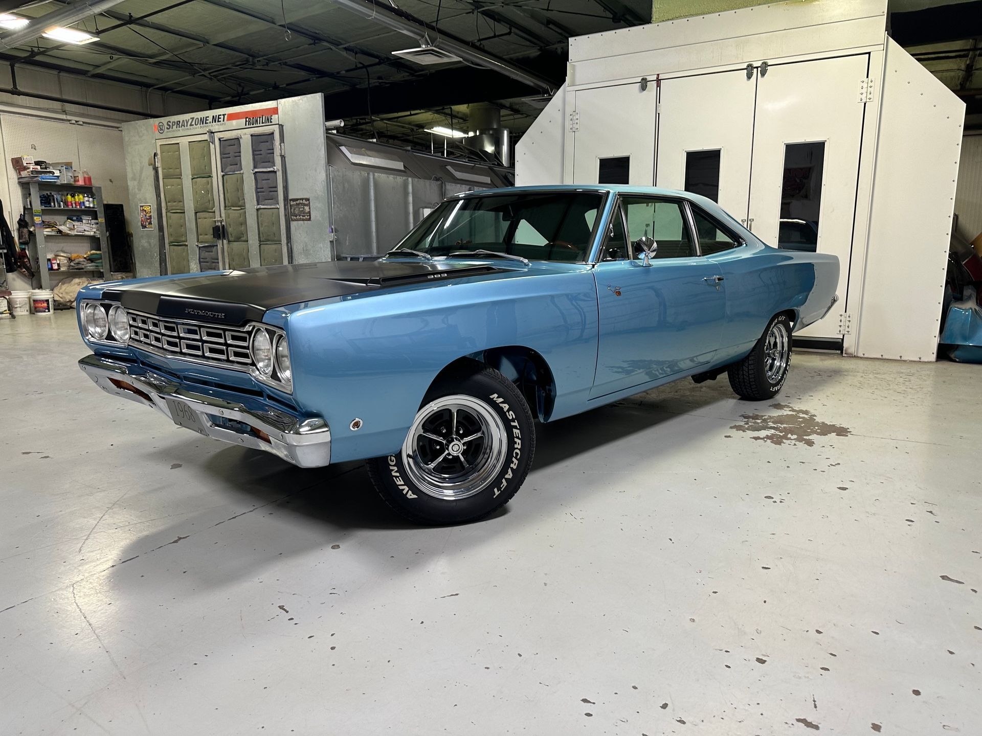 A blue car is parked in a garage next to a paint booth.