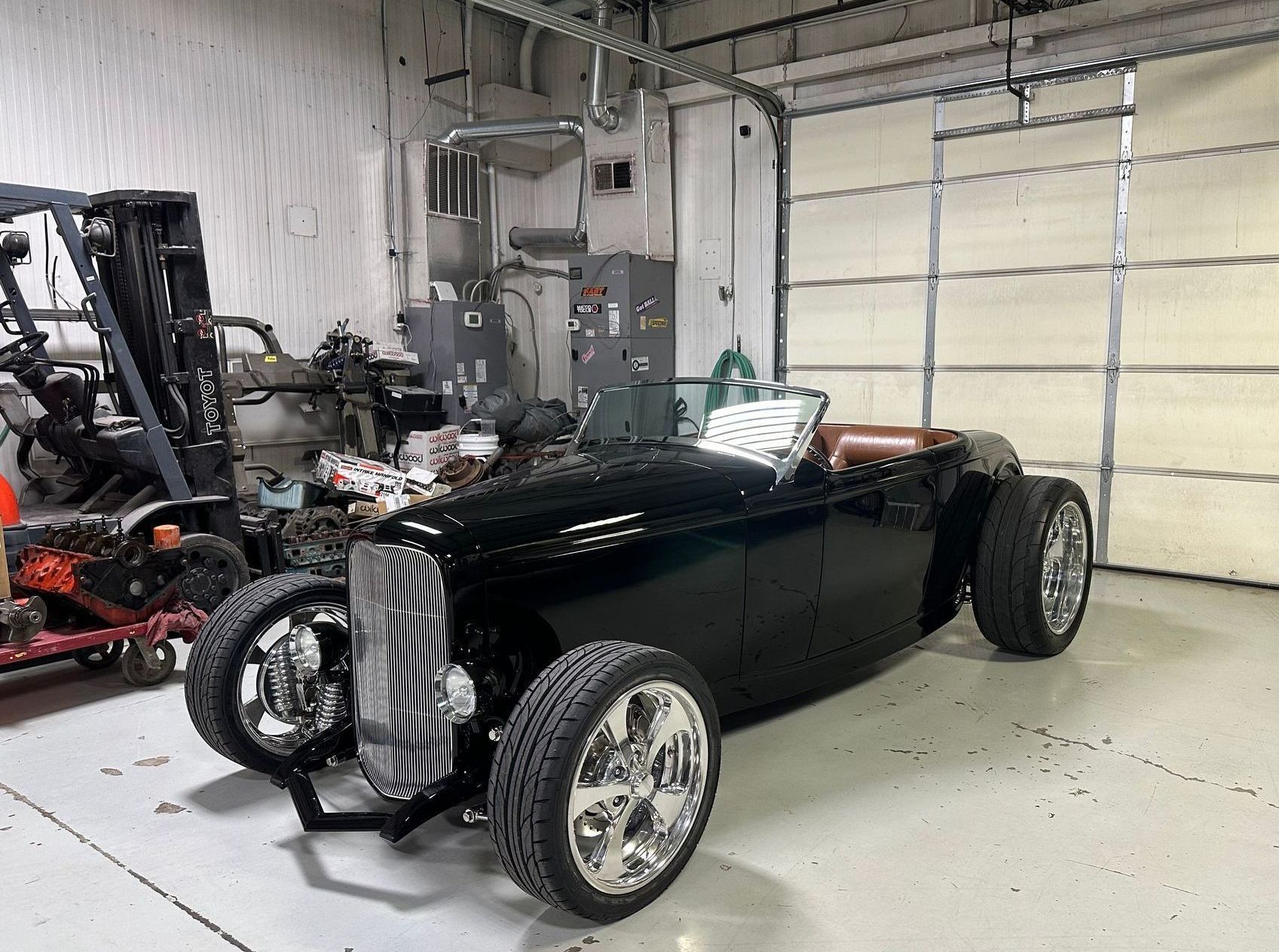 A black car is parked in a garage next to a forklift.