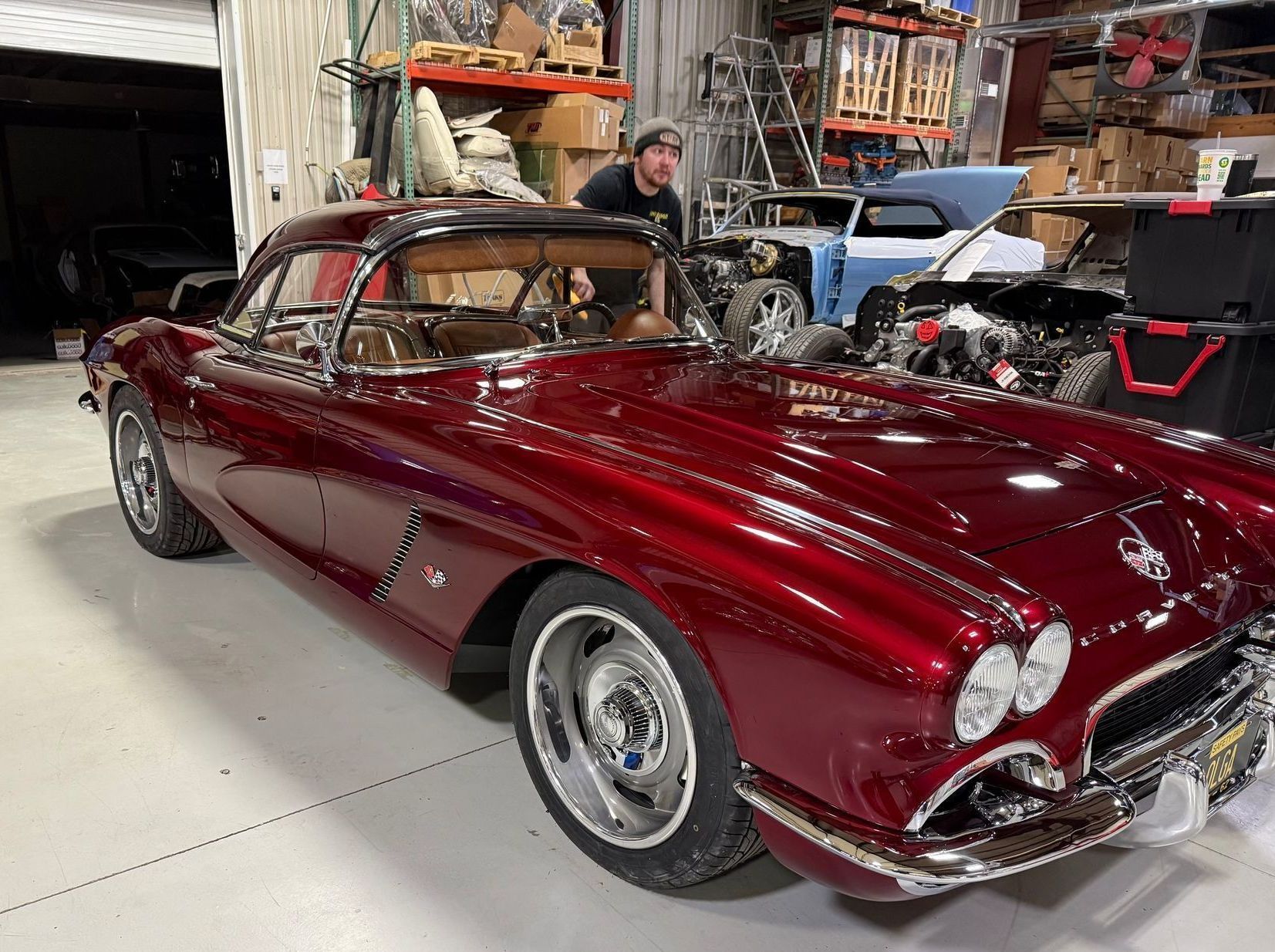 A man is sitting in a red corvette in a garage.