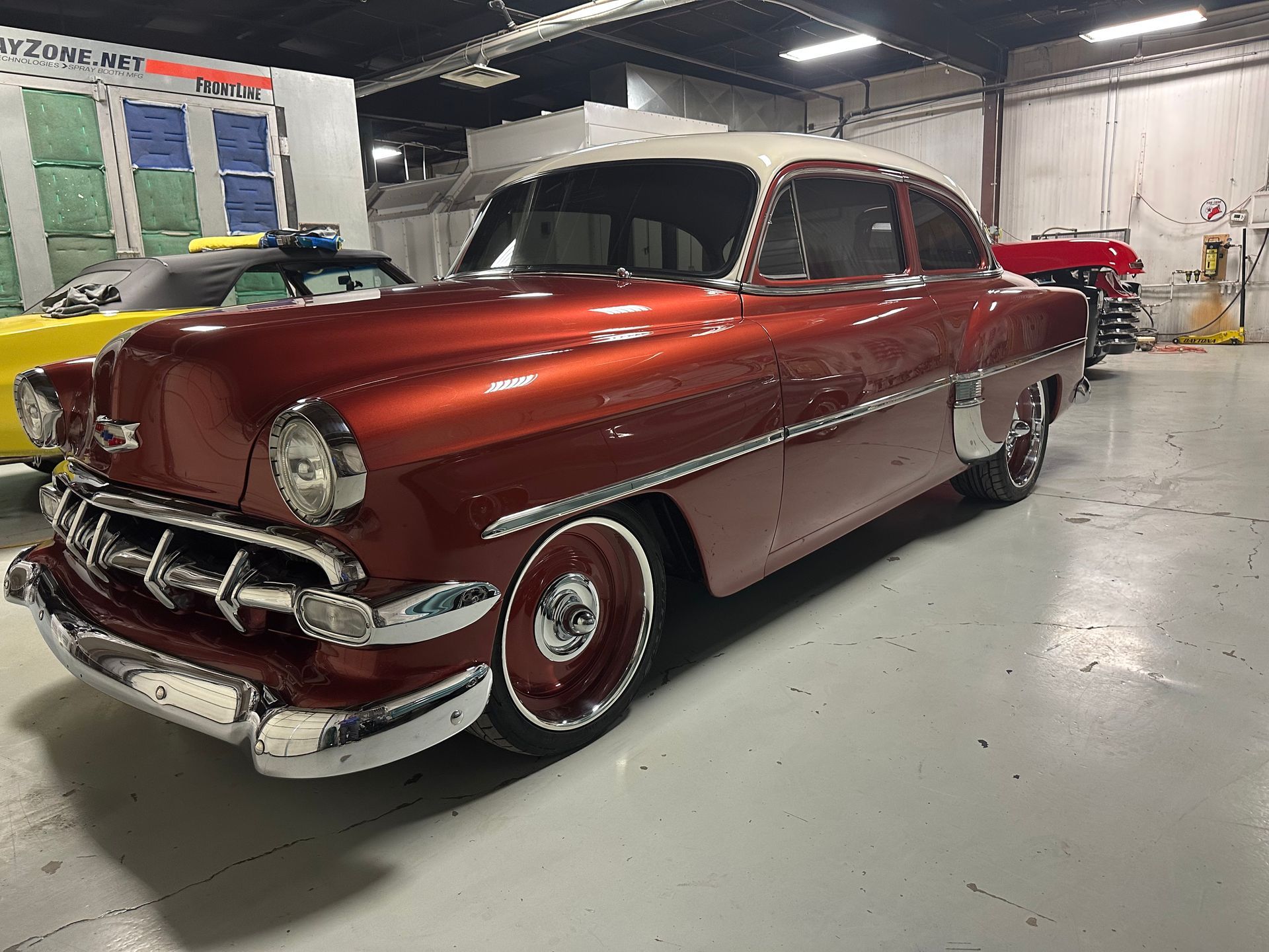 A red car is parked in a garage next to a yellow car.