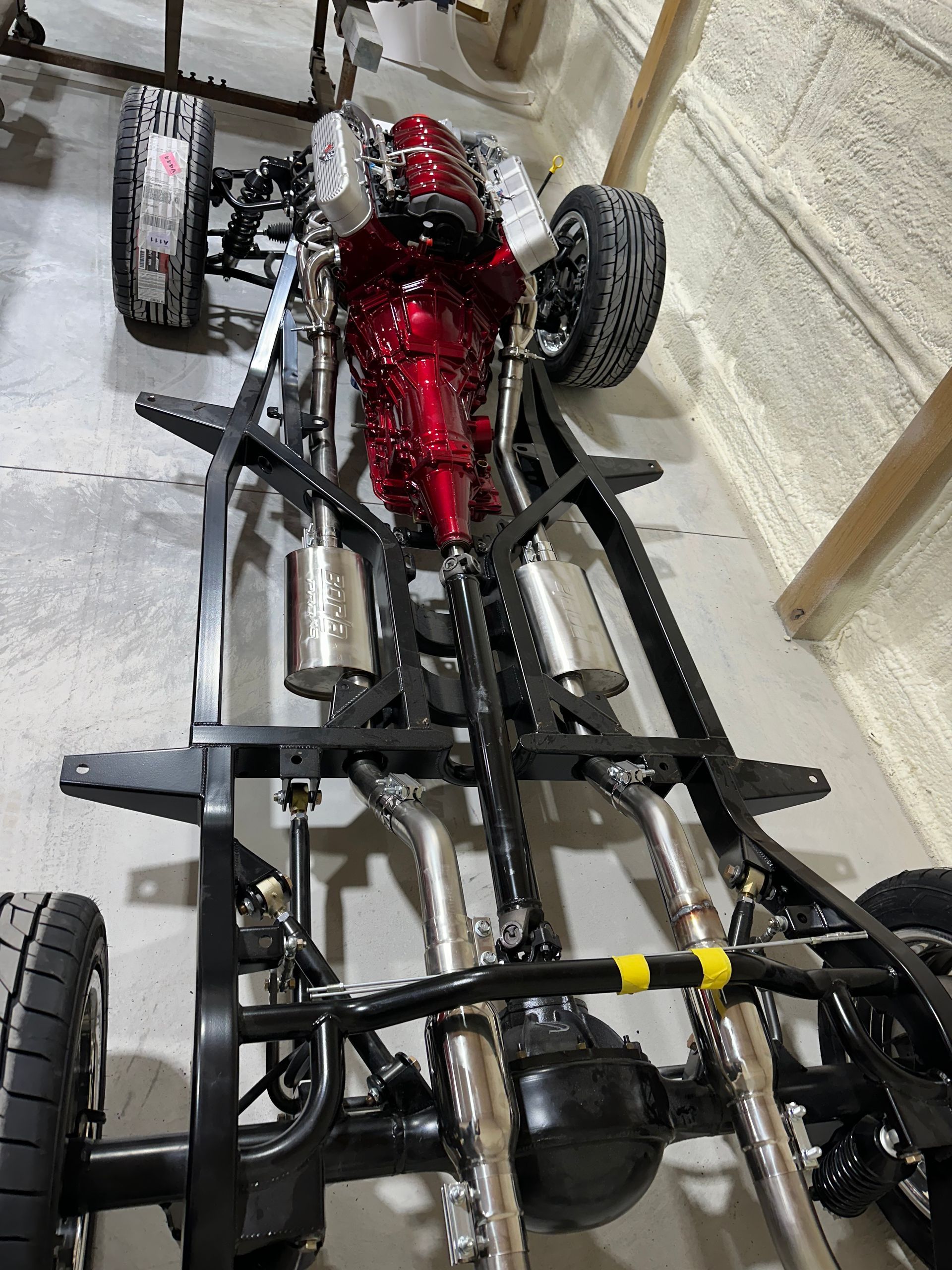 A car chassis with a red engine is sitting in a garage.