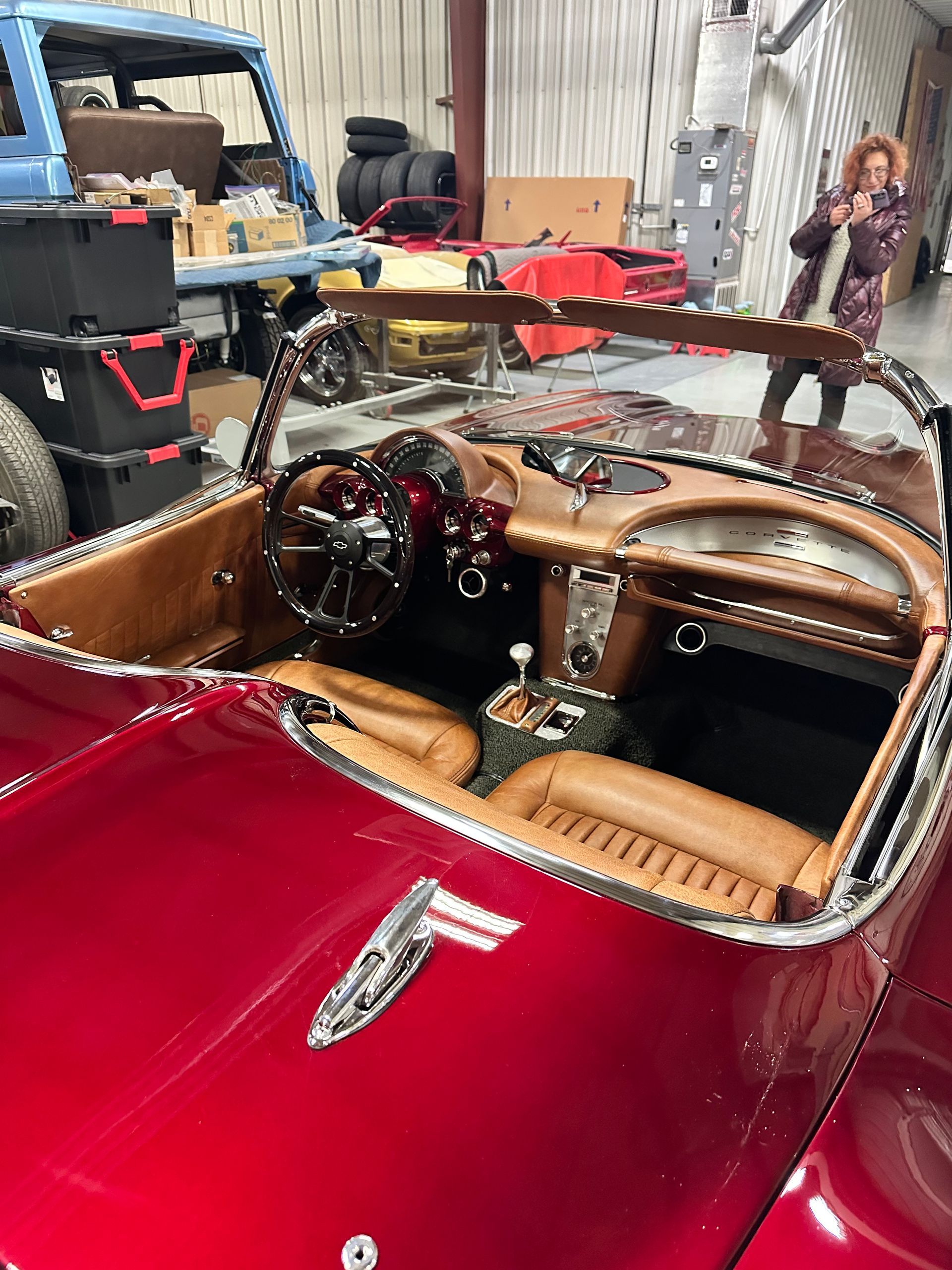 A woman is taking a picture of a red sports car in a garage.
