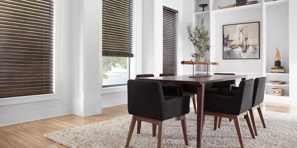 Modern dining room with dark chairs, a wooden table, blinds, and wall art