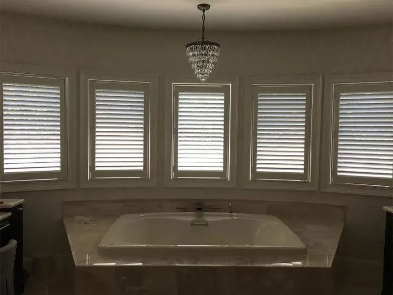 Curved bathroom alcove with a bathtub under five window blinds and a hanging pendant light
