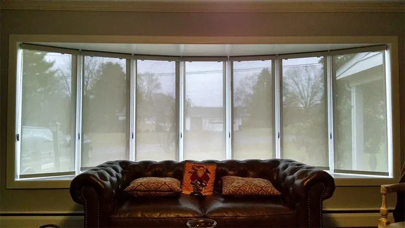 Living room with a dark sofa in front of a large bay window and sheer curtains