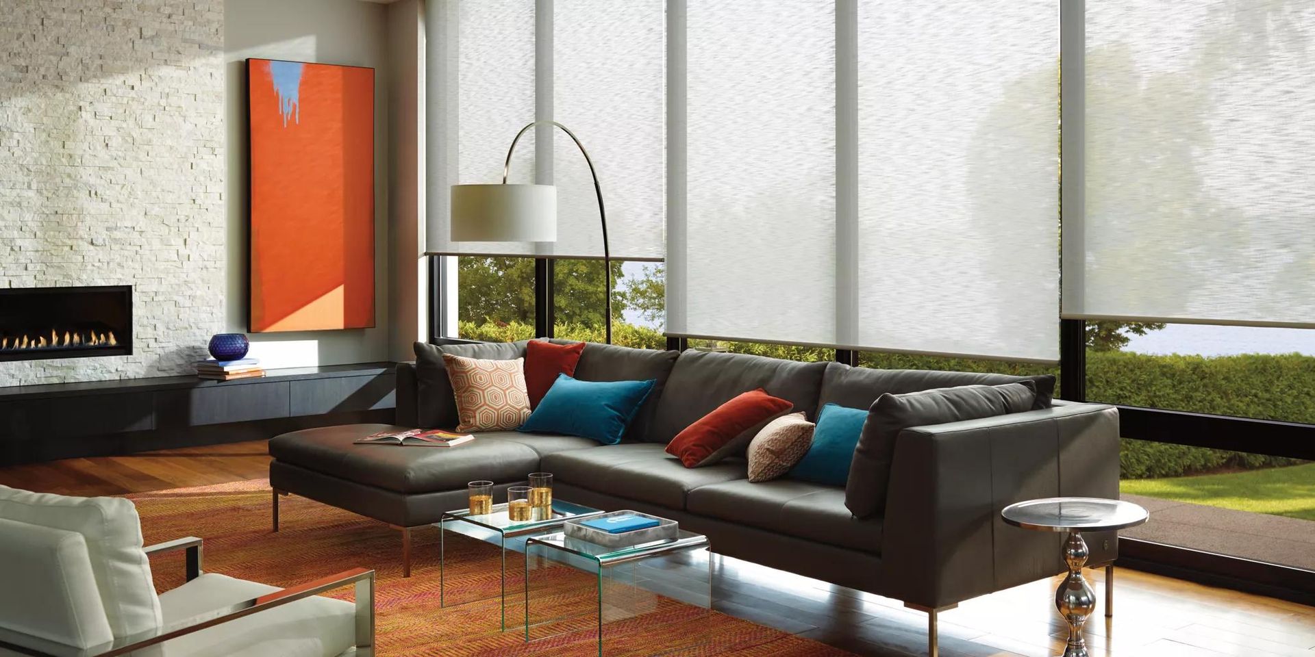 Modern living room with gray sofa, red and teal pillows, wood table, and floor-to-ceiling windows.