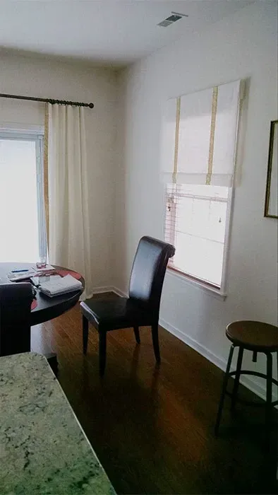 Small dining area with a chair, table, stool, and window blinds by a carpeted wall.