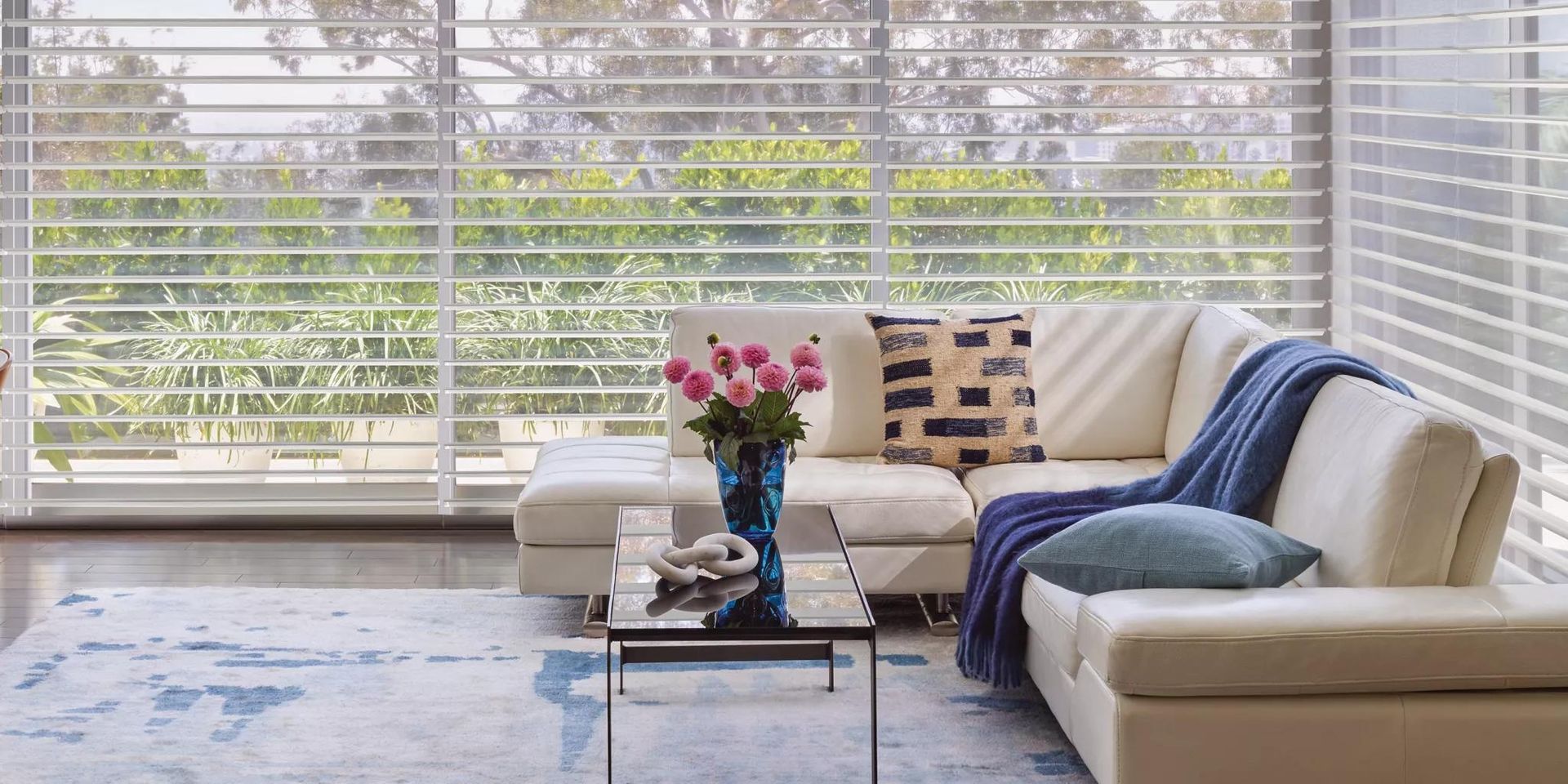 Bright living room with large windows, white sofa, blue throw, coffee table, and a patterned rug