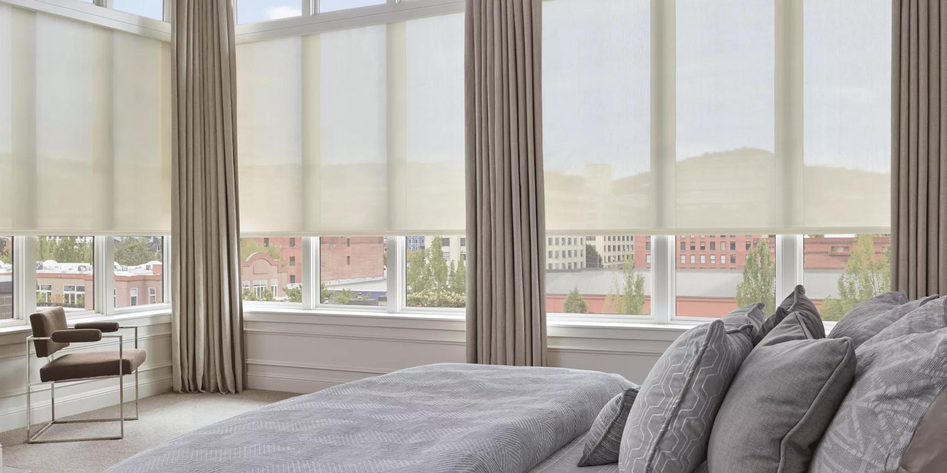 Bright bedroom with a large bed, floor-to-ceiling windows, and a city view