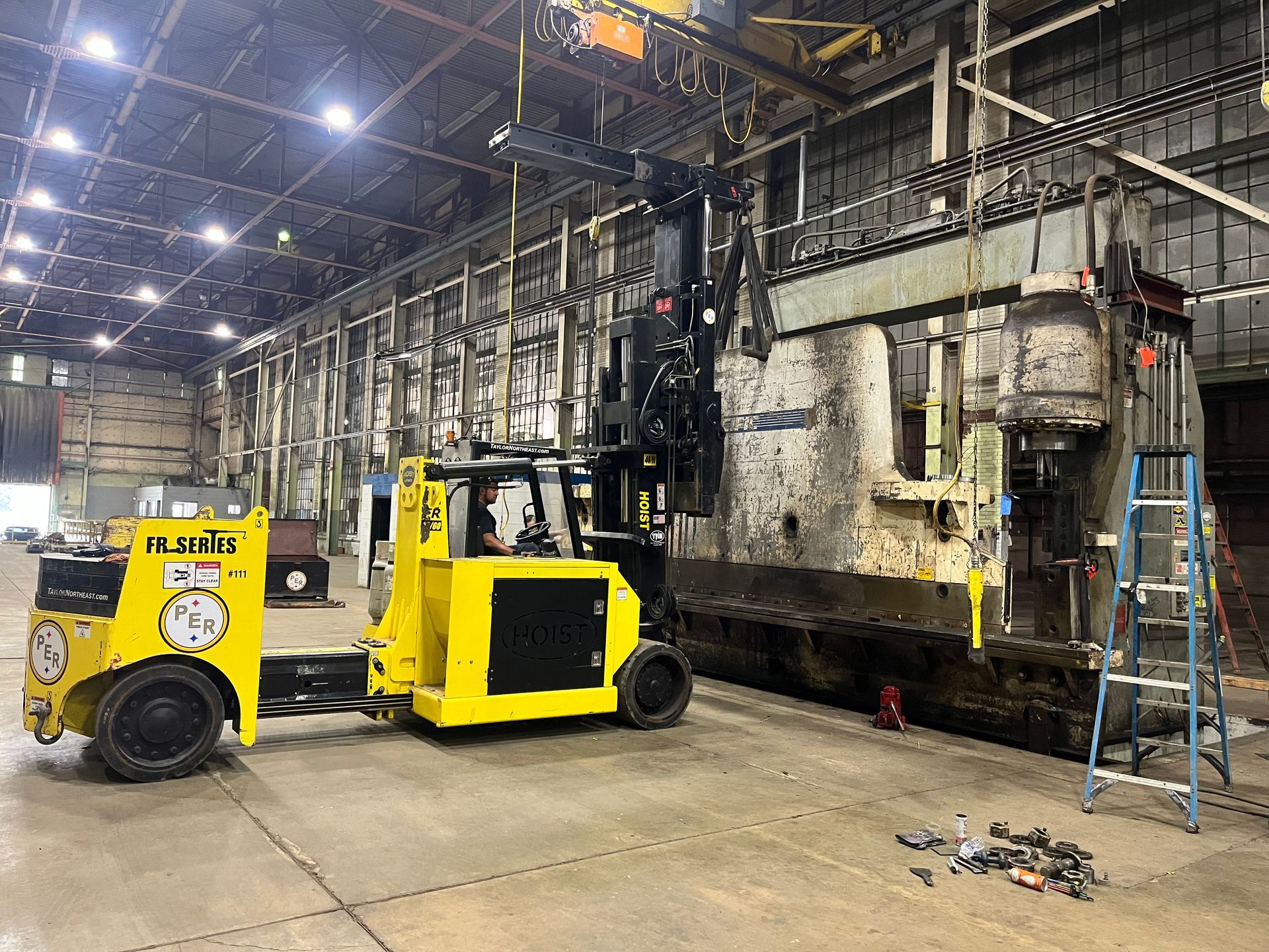 A yellow forklift is moving a large piece of metal in a warehouse.