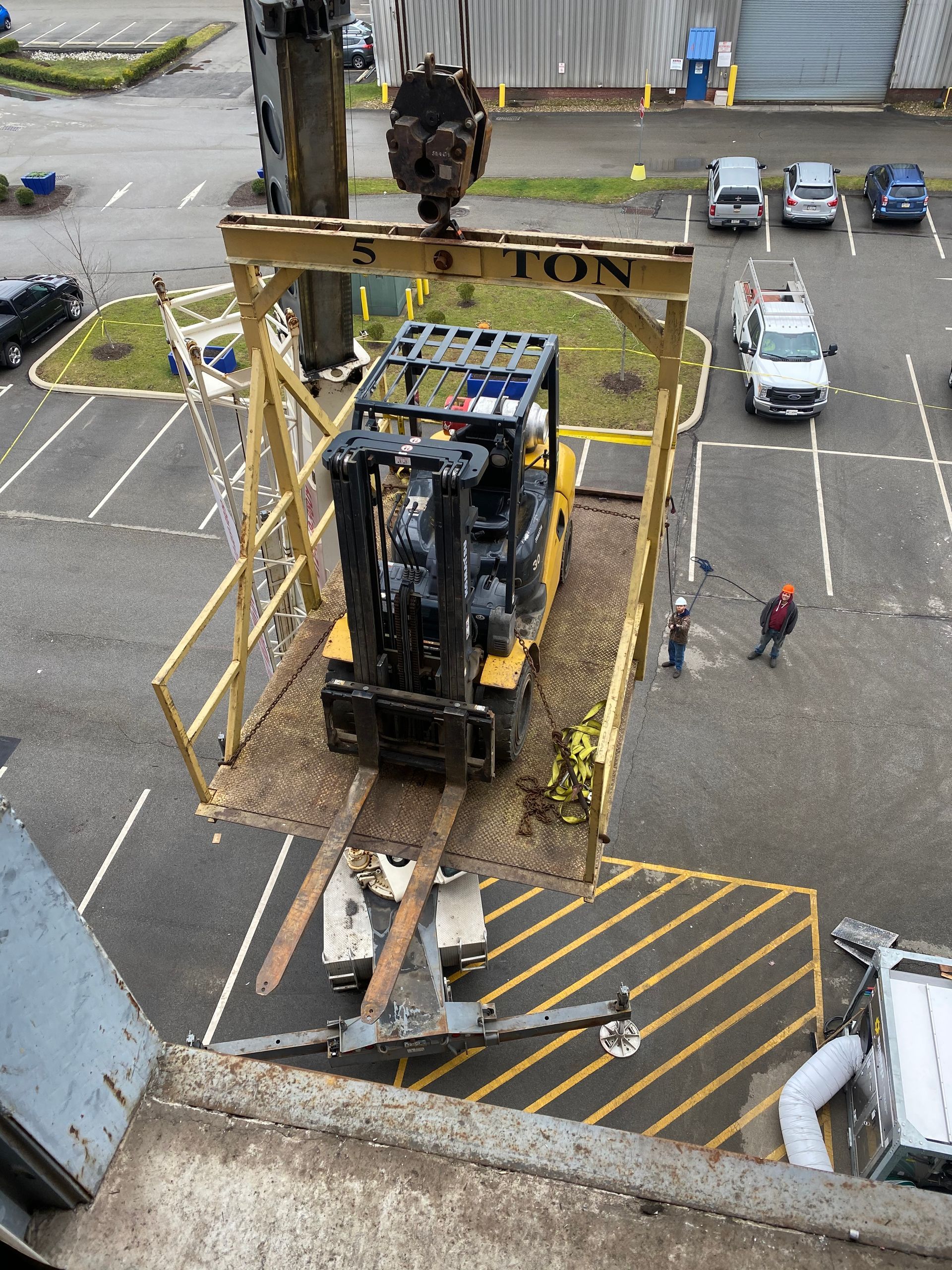 A forklift is being lifted by a crane in a parking lot