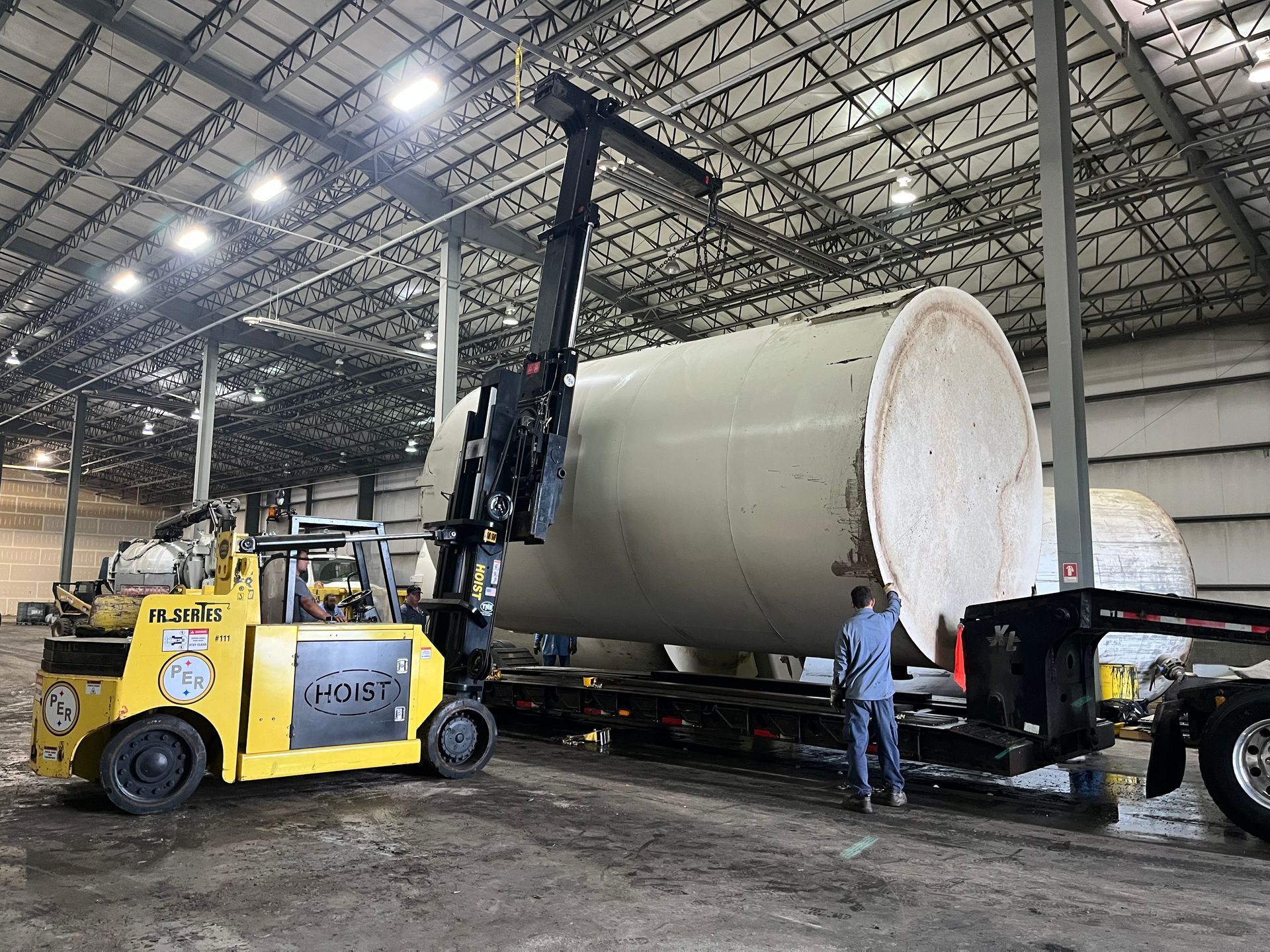 A large cylinder is being lifted by a forklift in a warehouse.